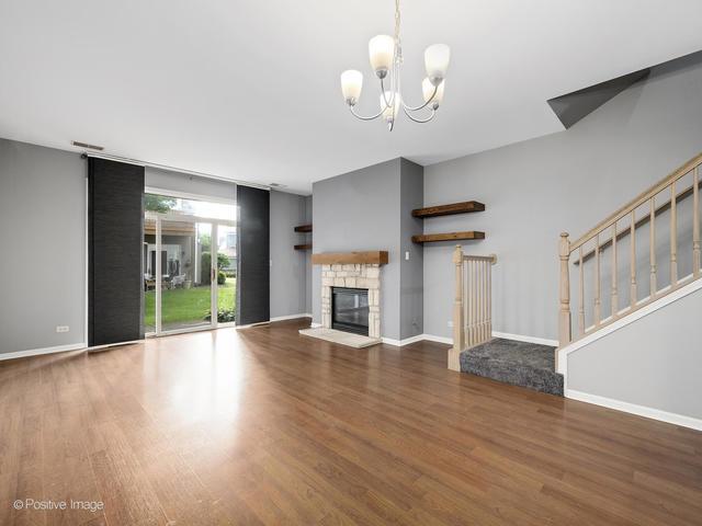 835 Genesee Dr, Naperville, IL 60563 - unfurnished living room featuring wood finished floors, a chandelier, a stone fireplace, and stairs