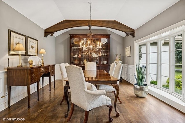 dining area with a chandelier, lofted ceiling, dark wood-style flooring, a wainscoted wall, and a decorative wall