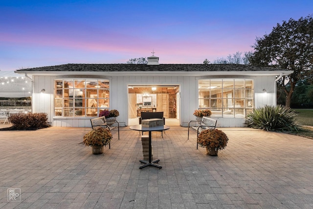 rear view of property featuring a patio area, a chimney, and board and batten siding