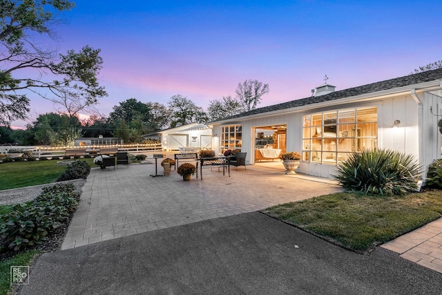 back of property with a patio area, board and batten siding, a chimney, and a yard