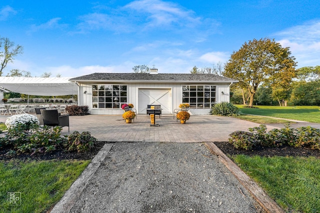 rear view of house featuring board and batten siding, a lawn, a chimney, and a patio area