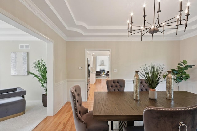 1123 Thackery Ln, Naperville, IL 60564 - dining space with a chandelier, a raised ceiling, light wood-style flooring, a wainscoted wall, and ornamental molding