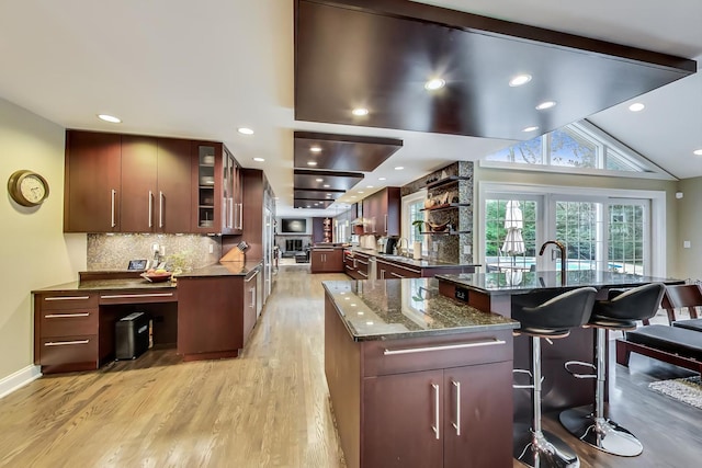1194 Oxford Ct, Highland Park, IL 60035 - kitchen with light wood-style flooring, a breakfast bar area, decorative backsplash, glass insert cabinets, and dark stone countertops