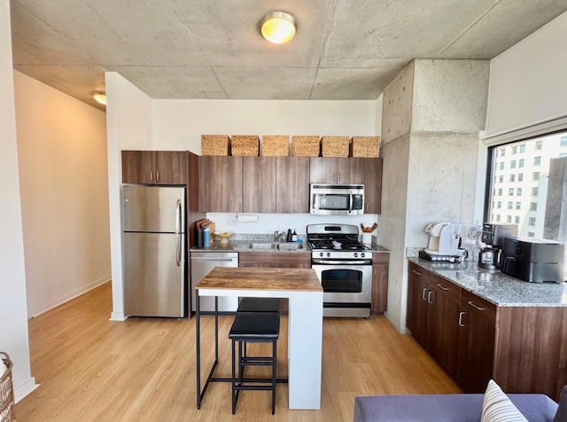 235 W Van Buren St Unit 1703, Chicago, IL 60607 - kitchen featuring appliances with stainless steel finishes, light wood-style floors, a kitchen breakfast bar, light stone counters, and a center island