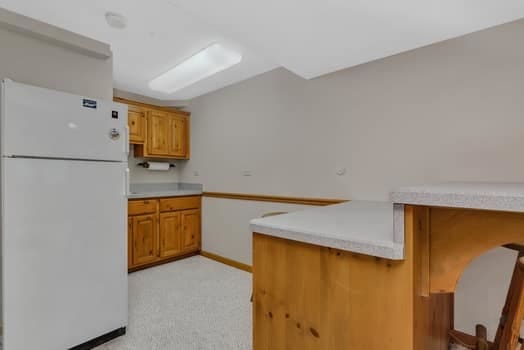 16620 Grants Trl, Orland Park, IL 60467 - kitchen with freestanding refrigerator, a peninsula, brown cabinetry, light countertops, and a breakfast bar area