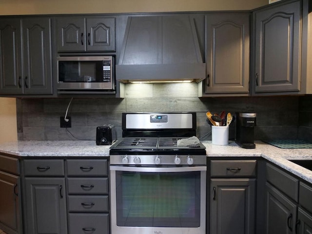 26 N Deer Lk, Villa Grove, IL 61956 - kitchen with appliances with stainless steel finishes, gray cabinets, extractor fan, tasteful backsplash, and light stone countertops