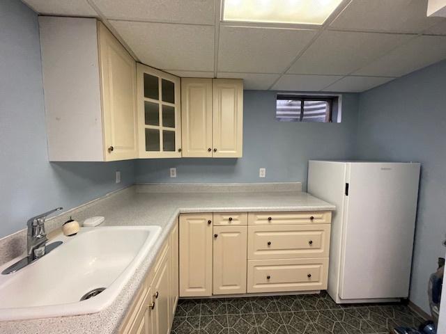 512 Tana Ln, Joliet, IL 60435 - kitchen with freestanding refrigerator, a paneled ceiling, light countertops, glass insert cabinets, and dark flooring