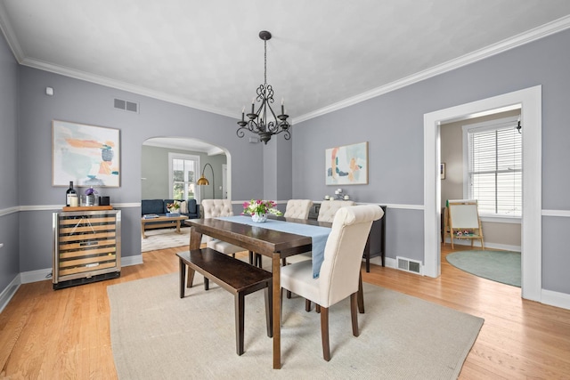 1718 Lake Ave, Wilmette, IL 60091 - dining area featuring arched walkways, wine cooler, light wood-style flooring, crown molding, and a chandelier