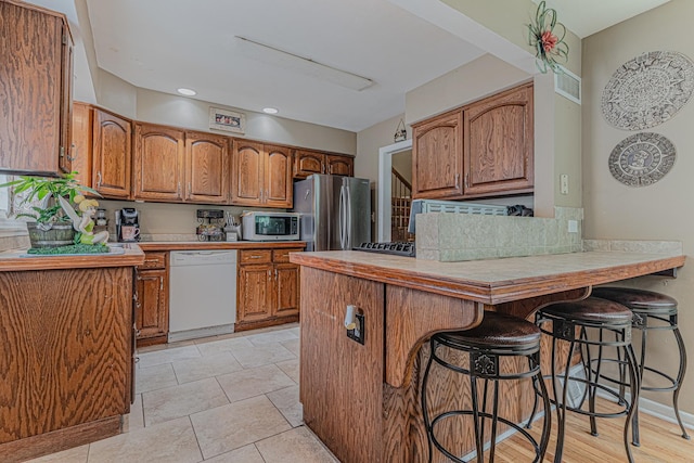 374 Heine Ave, Elgin, IL 60123 - kitchen with appliances with stainless steel finishes, a peninsula, brown cabinets, a kitchen breakfast bar, and backsplash