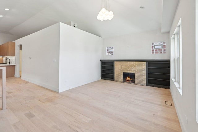 7930 S Kenwood Ave, Chicago, IL 60619 - unfurnished living room featuring light wood-style flooring, a brick fireplace, a chandelier, and high vaulted ceiling