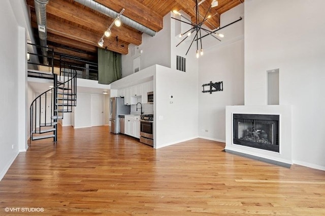 2614 N Clybourn Ave Unit 311, Chicago, IL 60614 - unfurnished living room featuring a towering ceiling, stairway, light wood finished floors, a chandelier, and a wooden ceiling with exposed beams