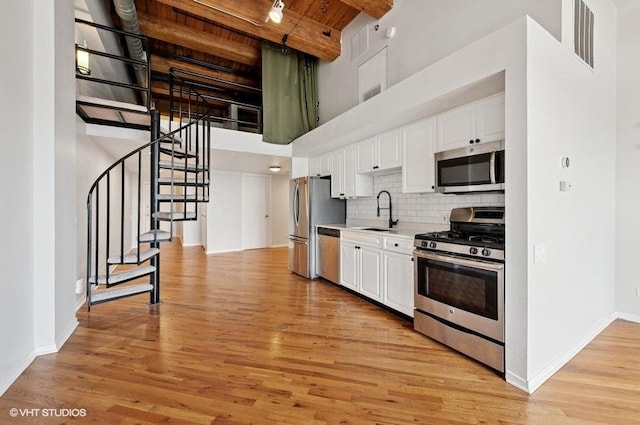 2614 N Clybourn Ave Unit 311, Chicago, IL 60614 - kitchen featuring appliances with stainless steel finishes, a towering ceiling, white cabinetry, light countertops, and light wood-style flooring