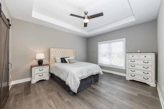 561 Sudbury Cir, Oswego, IL 60543 - bedroom with a barn door, a raised ceiling, dark wood-style floors, and a ceiling fan