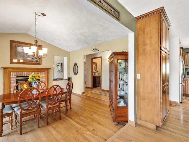12828 Menominee Trl, Roscoe, IL 61073 - dining area featuring a brick fireplace, light wood finished floors, a chandelier, and vaulted ceiling