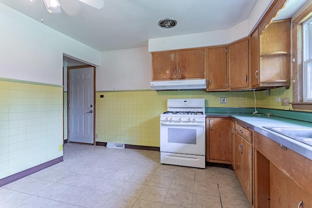 1481 Bloomingdale Rd, Glendale Heights, IL 60139 - kitchen featuring gas range gas stove, under cabinet range hood, tile walls, brown cabinets, and light tile patterned flooring