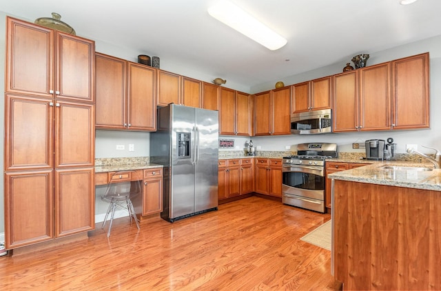 140 S River St Unit 307, Aurora, IL 60506 - kitchen featuring appliances with stainless steel finishes, brown cabinetry, light wood-type flooring, and light stone countertops