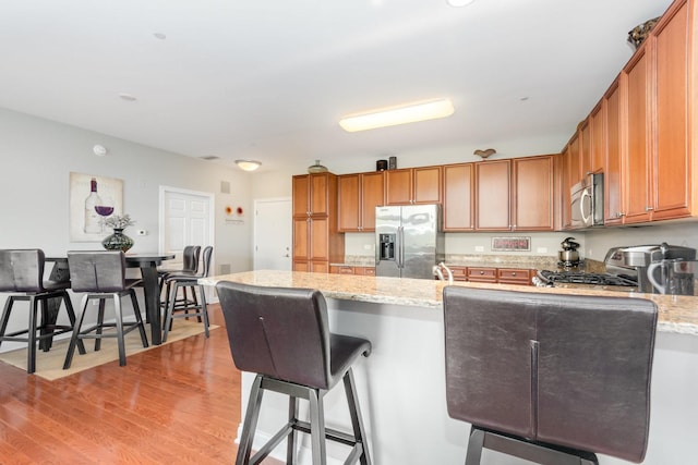 140 S River St Unit 307, Aurora, IL 60506 - kitchen with stainless steel appliances, a peninsula, light stone counters, and brown cabinetry