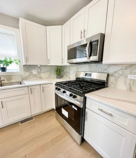 9302 S Eberhart Ave, Chicago, IL 60619 - kitchen featuring stainless steel appliances, white cabinets, light wood finished floors, decorative backsplash, and light countertops