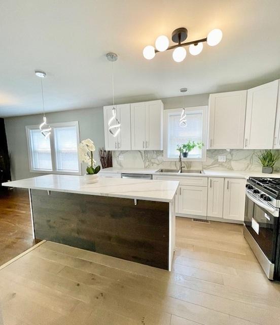 9302 S Eberhart Ave, Chicago, IL 60619 - kitchen featuring appliances with stainless steel finishes, light wood-style flooring, white cabinets, a kitchen island, and tasteful backsplash