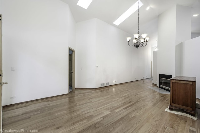 20739 N Weiland Rd, Prairie View, IL 60069 - unfurnished living room with high vaulted ceiling, a chandelier, light wood-type flooring, a skylight, and a fireplace with flush hearth