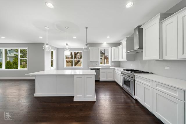 1122 W Wilson St, Palatine, IL 60067 - kitchen with wall chimney exhaust hood, stainless steel appliances, a kitchen island, light countertops, and dark wood finished floors