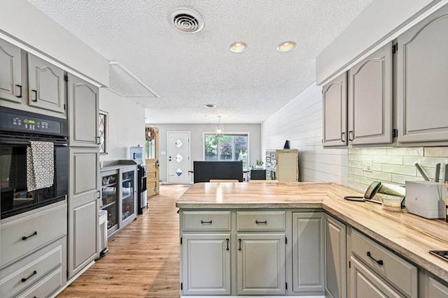 412 E S St, Peotone, IL 60468 - kitchen featuring oven, a peninsula, gray cabinetry, a textured ceiling, and light wood finished floors