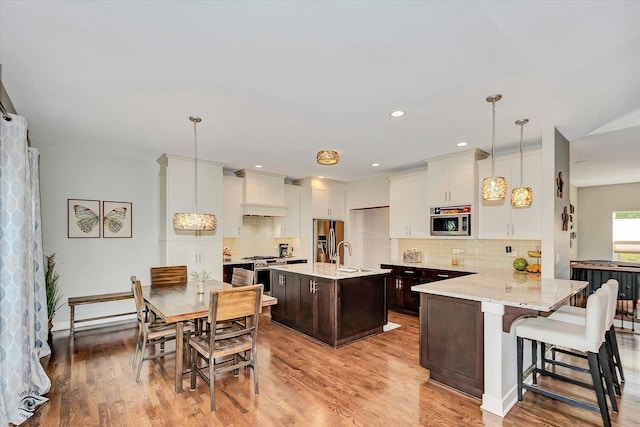 24401 S Clydesdale Ct, Manhattan, IL 60442 - kitchen featuring appliances with stainless steel finishes, dark brown cabinetry, decorative backsplash, light wood finished floors, and a kitchen island with sink