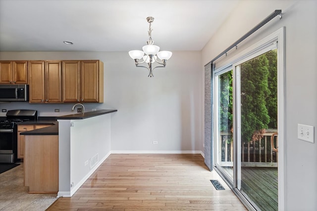 627 S Jade Ln, Round Lake, IL 60073 - kitchen with appliances with stainless steel finishes, dark countertops, a peninsula, light wood finished floors, and a chandelier