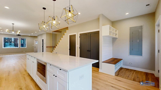 300 N Lockwood Ave, Chicago, IL 60644 - kitchen with electric panel, a chandelier, stainless steel microwave, light wood-type flooring, and white cabinets