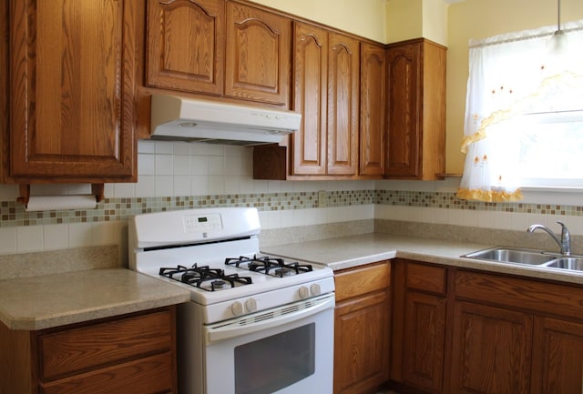 316 Marguerite St, Elgin, IL 60123 - kitchen featuring white gas range, under cabinet range hood, brown cabinetry, decorative backsplash, and light countertops