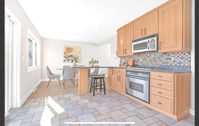1933 Birch St, Des Plaines, IL 60018 - kitchen featuring appliances with stainless steel finishes, stone finish floors, decorative backsplash, a kitchen breakfast bar, and light brown cabinetry