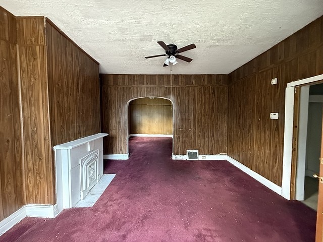 6044 S Justine St, Chicago, IL 60636 - empty room featuring ceiling fan, arched walkways, a textured ceiling, wooden walls, and carpet