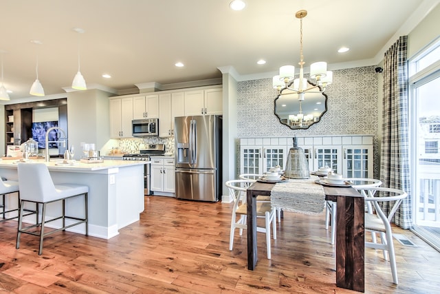 1552 Times Dr, Des Plaines, IL 60018 - kitchen with appliances with stainless steel finishes, a chandelier, wallpapered walls, a kitchen breakfast bar, and white cabinetry