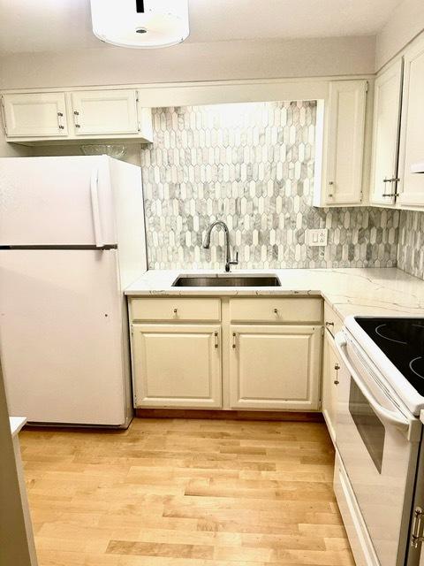 2317 N Neva Ave Unit 106A, Chicago, IL 60707 - kitchen featuring white appliances, light wood-style floors, light stone countertops, decorative backsplash, and white cabinetry