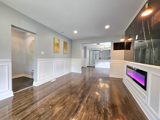 8109 S Marquette Ave, Chicago, IL 60617 - unfurnished living room featuring dark wood-style floors, a glass covered fireplace, a decorative wall, a wainscoted wall, and recessed lighting
