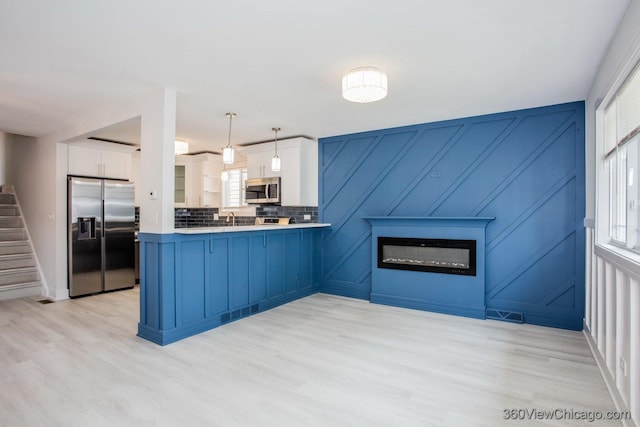 9154 S Luella Ave, Chicago, IL 60617 - kitchen featuring stainless steel appliances, white cabinetry, a glass covered fireplace, light wood finished floors, and a peninsula