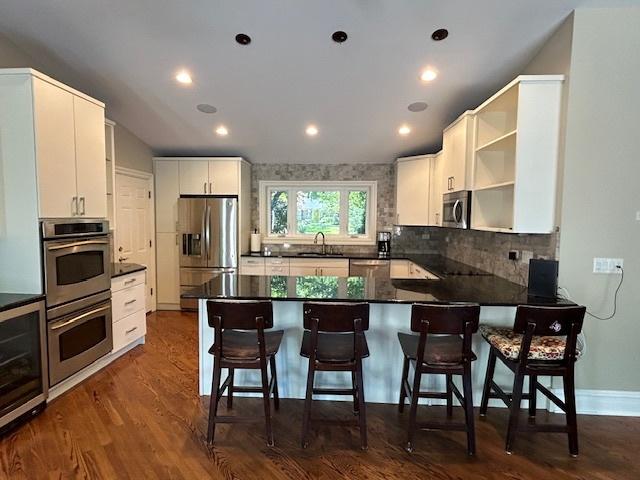 2277 S Westwood Ln, Palatine, IL 60067 - kitchen featuring appliances with stainless steel finishes, open shelves, a peninsula, dark countertops, and backsplash