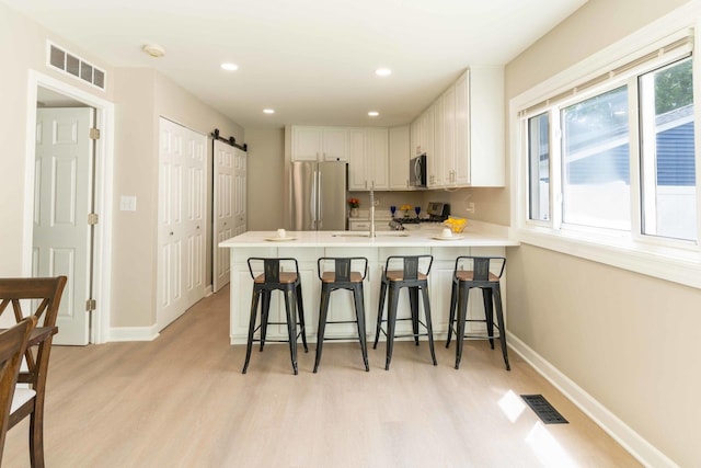 129 Highbury Dr, Elgin, IL 60120 - kitchen featuring stainless steel appliances, a barn door, a peninsula, light wood-style floors, and white cabinetry