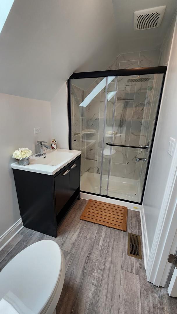 3039 S Kolin Ave, Chicago, IL 60623 - bathroom featuring wood finished floors, vanity, vaulted ceiling, and a stall shower