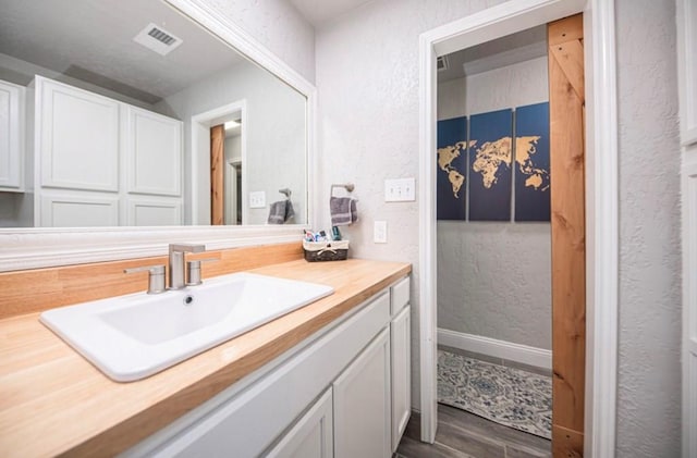 bathroom with baseboards, visible vents, a textured wall, wood finished floors, and vanity