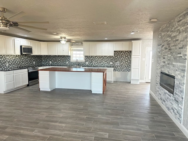 kitchen with a fireplace, stainless steel appliances, dark countertops, backsplash, and white cabinets