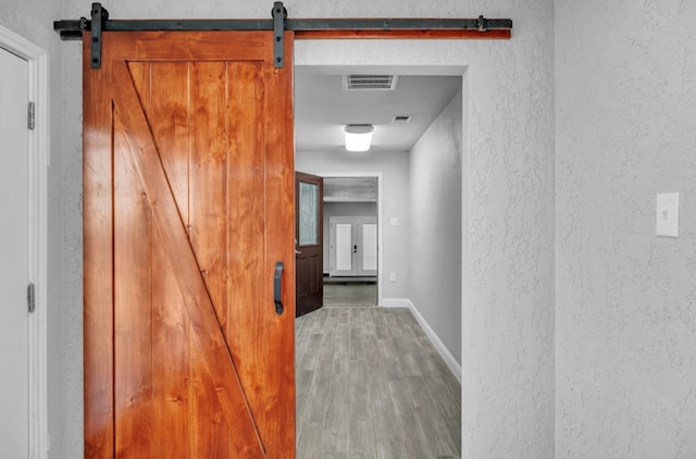 corridor with a textured wall, a barn door, wood finished floors, and visible vents