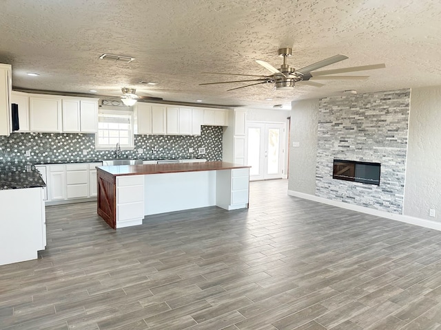 kitchen with a stone fireplace, wood finished floors, white cabinetry, a center island, and dark countertops