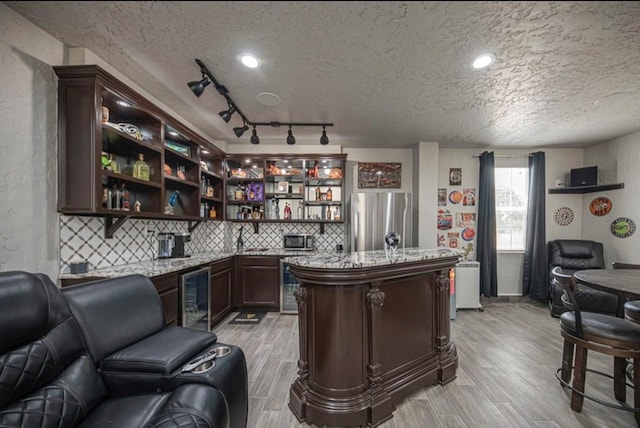 bar featuring wine cooler, backsplash, appliances with stainless steel finishes, wood tiled floor, and a textured ceiling