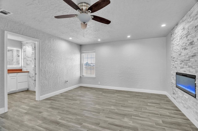 unfurnished bedroom featuring a fireplace, light wood finished floors, visible vents, a textured wall, and a textured ceiling