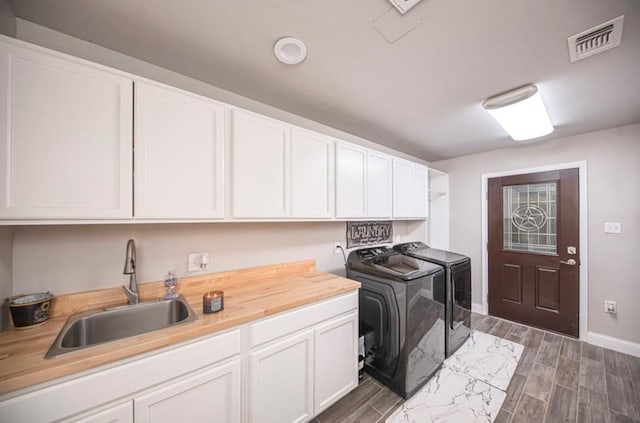 clothes washing area with visible vents, cabinet space, washing machine and dryer, wood tiled floor, and a sink