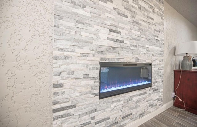 room details featuring wood finish floors, a stone fireplace, and baseboards