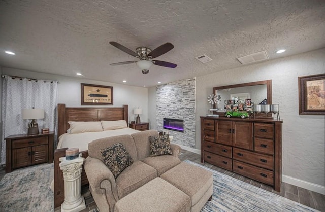 bedroom with a textured ceiling, a textured wall, a fireplace, wood finished floors, and visible vents