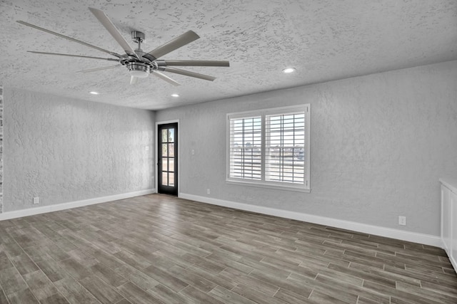 empty room with a textured wall, baseboards, wood finished floors, and recessed lighting