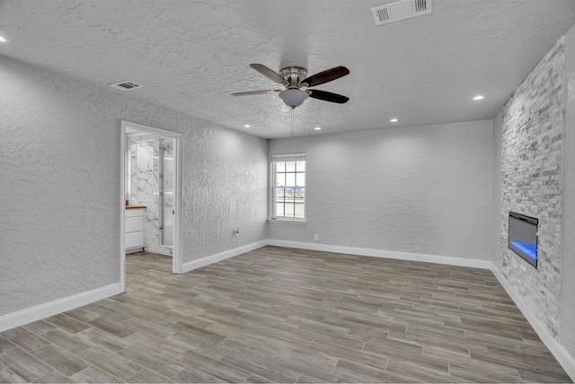 empty room with a textured wall, visible vents, light wood-style floors, and a stone fireplace